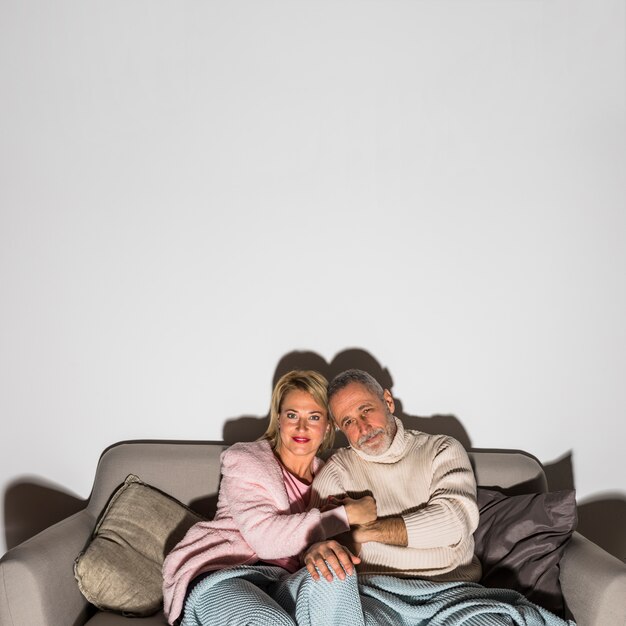 Homme âgé, main dans la main avec une femme et regardant la télévision sur un canapé