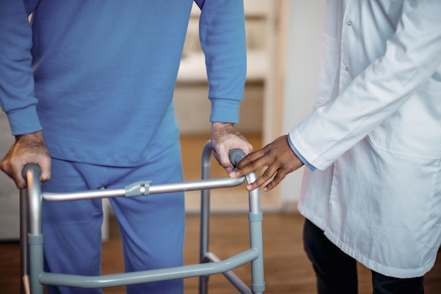 Homme âgé méconnaissable aidé à marcher avec un déambulateur de mobilité dans une maison de retraite