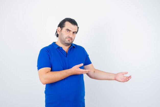 Homme d'âge moyen accueillant quelque chose en t-shirt bleu et l'air confiant. vue de face.
