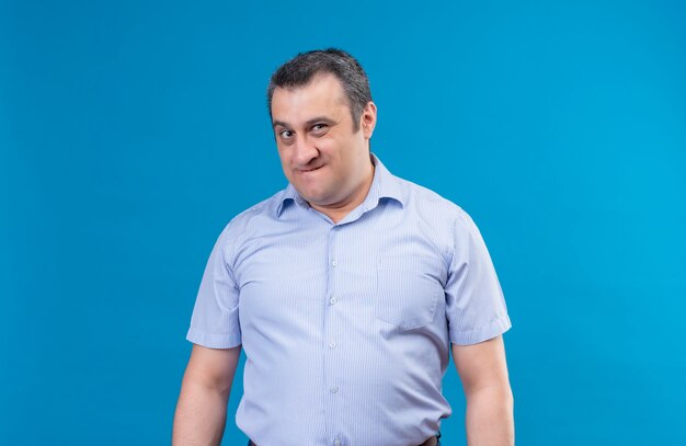 Homme d'âge moyen agacé en chemise bleue regardant la caméra avec une expression mécontente sur un espace bleu