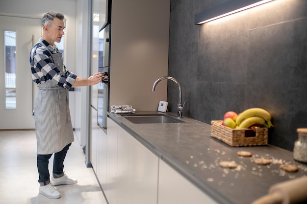 Homme d'âge moyen attentif dans des vêtements décontractés touchant le panneau de commande du four dans la cuisine