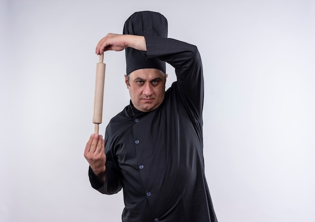 Homme d'âge moyen cuisinier en uniforme de chef tenant le rouleau à pâtisserie sur un mur blanc isolé avec copie espace