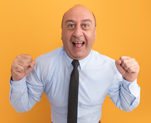 Homme d'âge moyen excité portant un t-shirt blanc avec une cravate montrant un geste oui isolé sur un mur orange