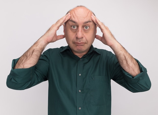 Homme d'âge moyen fatigué portant un t-shirt vert mettant les mains sur le temple isolé sur mur blanc