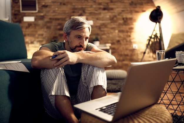 Homme d'âge moyen lisant un e-mail tout en travaillant tard sur un ordinateur portable à la maison