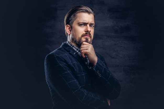 Homme d'âge moyen pensif avec barbe et coiffure vêtu d'un élégant costume bleu sur fond sombre texturé en studio.