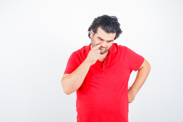Photo gratuite homme d'âge moyen poussant son nez en t-shirt rouge et à la vue réfléchie, de face.