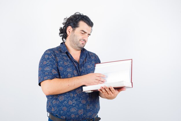 Homme d'âge moyen à la recherche de livre en chemise et à la vue de face, focalisée.