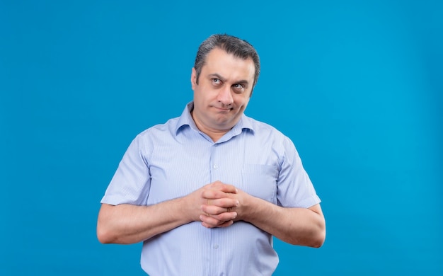 Homme d'âge moyen réfléchi en chemise à rayures bleues pensant et se frottant les mains ensemble sur un fond bleu