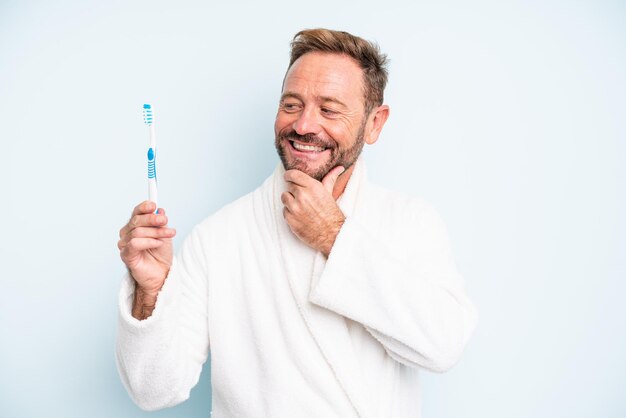 Homme d'âge moyen souriant avec une expression heureuse et confiante avec la main sur le menton. concept de brosse à dents