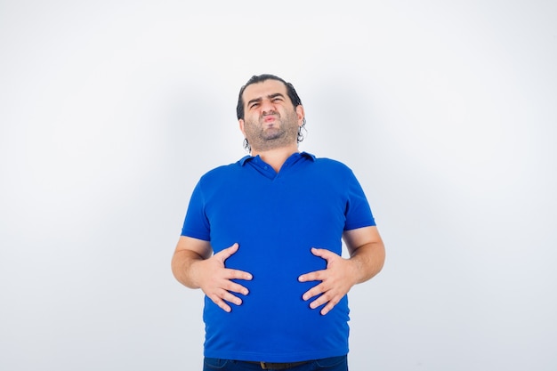 Photo gratuite homme d'âge moyen en t-shirt bleu avec les mains sur le ventre et ayant l'air malade