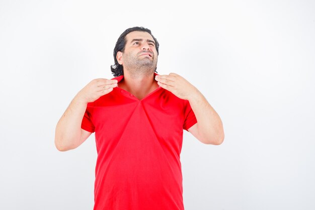 Homme D'âge Moyen En T-shirt Rouge Tenant Le Col Tout En Se Sentant Chaud Et à L'ennui, Vue De Face.