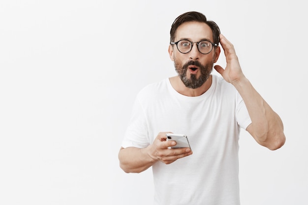 Homme d'âge mûr barbu excité et heureux posant avec son téléphone