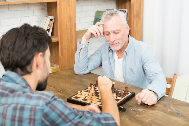 Photo gratuite homme âgé pensif et jeune homme jouant aux échecs à table près d'étagères