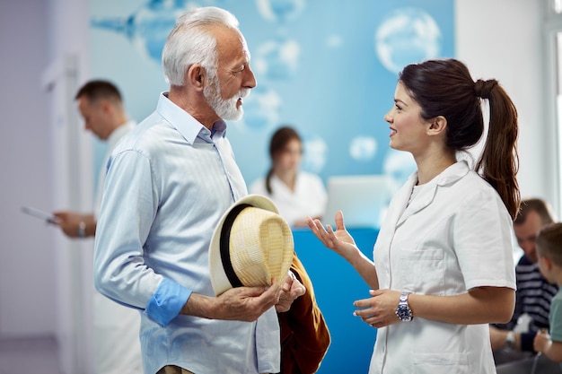 Homme âgé souriant communiquant avec une infirmière debout dans le hall d'une clinique médicale