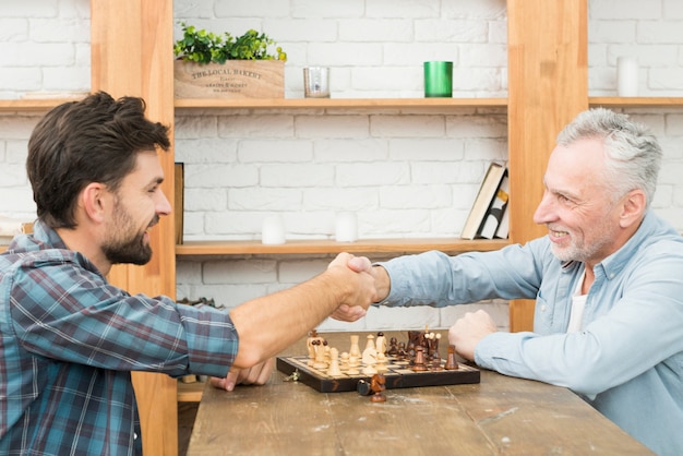 Photo gratuite homme âgé souriant et jeune homme se serrant la main à table avec un échiquier