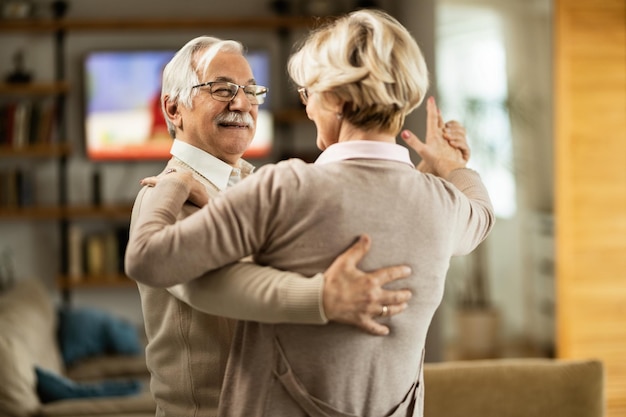 Homme âgé souriant et sa femme dansant à la maison