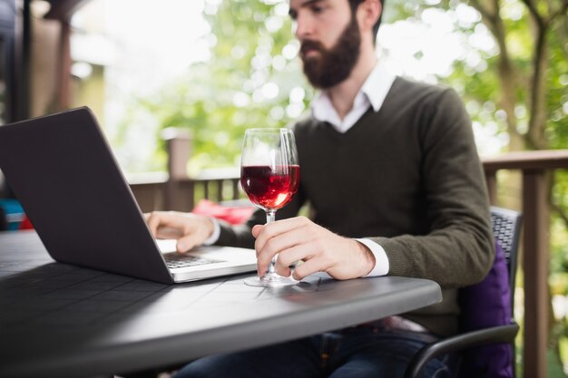 Homme à l'aide d'un ordinateur portable tout en ayant un verre de vin