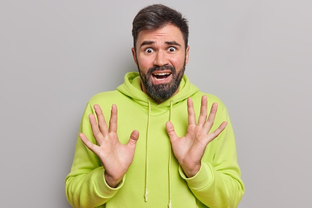 l'homme a l'air effrayé a des phobies soulève la paume essaie de se protéger de quelque chose d'affreux porte un sweat à capuche décontracté semble désespéré et dévasté isolé sur gris