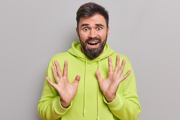 l'homme a l'air effrayé a des phobies soulève la paume essaie de se protéger de quelque chose d'affreux porte un sweat à capuche décontracté semble désespéré et dévasté isolé sur gris