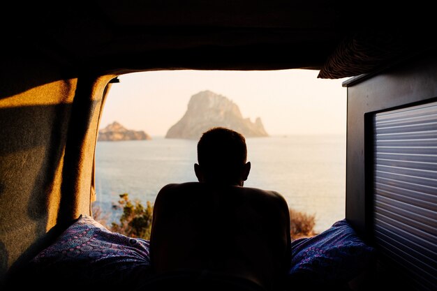 Homme allongé dans une caravane et profitant du coucher de soleil sur une plage