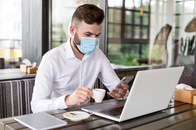 Homme à angle élevé avec masque travaillant à la terrasse