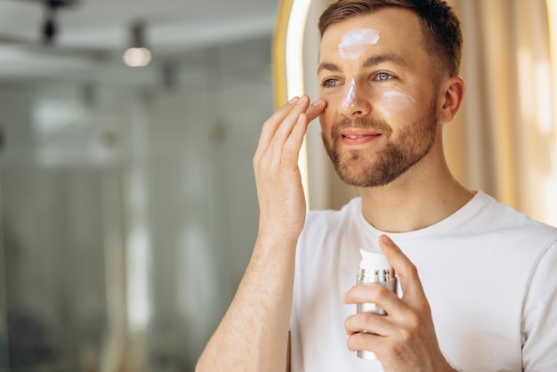 Homme appliquant de la crème pour le visage à la maison