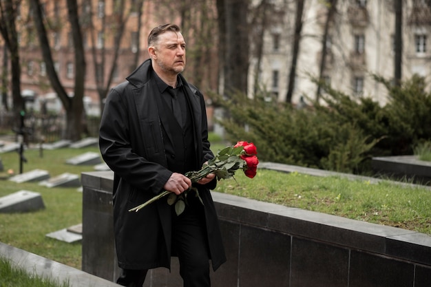 Photo gratuite homme apportant des roses à une pierre tombale au cimetière