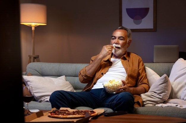 Photo gratuite homme appréciant la nourriture tout en étant seul à la maison et en regardant la télévision