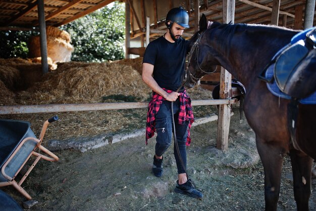 Homme arabe à grande barbe portant un casque noir avec un cheval arabe