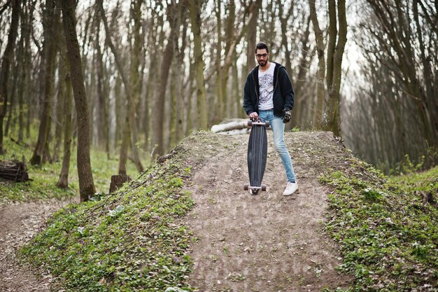 Homme arabe de style rue à lunettes avec longboard sur bois