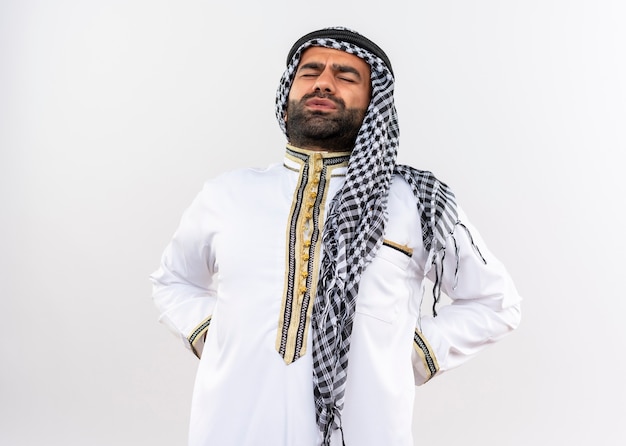 Photo gratuite l'homme arabe en usure traditionnelle toucher le dos à mal avoir la douleur debout sur un mur blanc