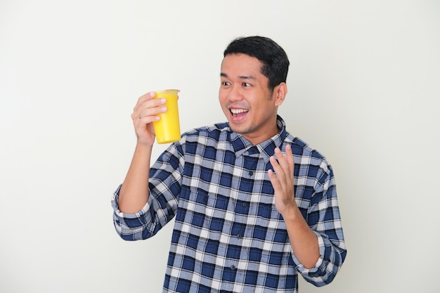 Homme asiatique adulte montrant le visage heureux en regardant une tasse de boisson froide de jus de fruit jaune