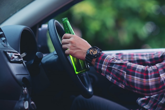 Photo gratuite homme asiatique détient une bouteille de bière tout en conduisant une voiture