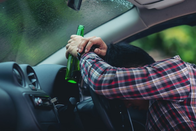 homme asiatique détient une bouteille de bière tout en conduisant une voiture