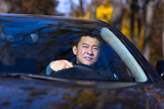 Un homme asiatique pensif est assis dans la voiture, le conducteur attend et est triste