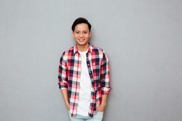 Homme asiatique souriant, debout sur un mur gris.