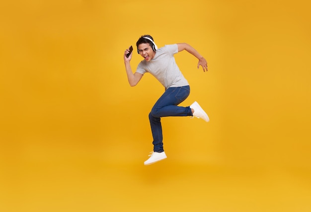 Homme asiatique souriant tenant un smartphone et sautant avec un casque sans fil écoutant de la musique