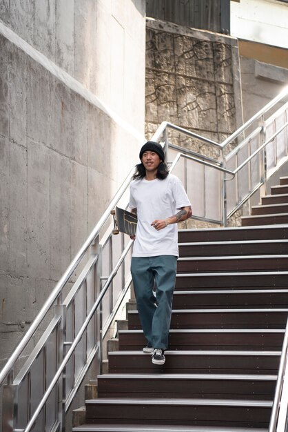 Homme asiatique tenant sa planche à roulettes en marchant dans les escaliers