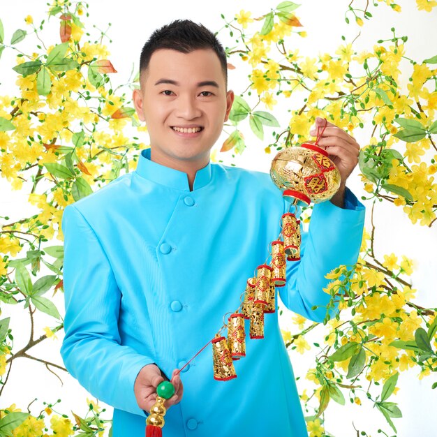 Homme asiatique en veste traditionnelle posant avec une lanterne colorée, entourée de mimosa en fleurs
