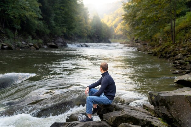 Homme assis au bord de la rivière vue latérale