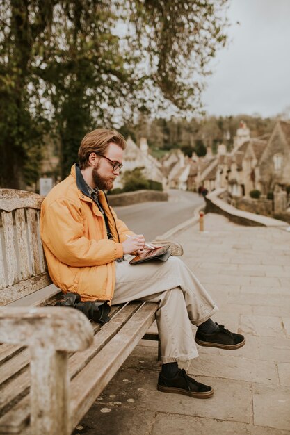 Homme assis sur un banc et travaillant sur tablette dans le village