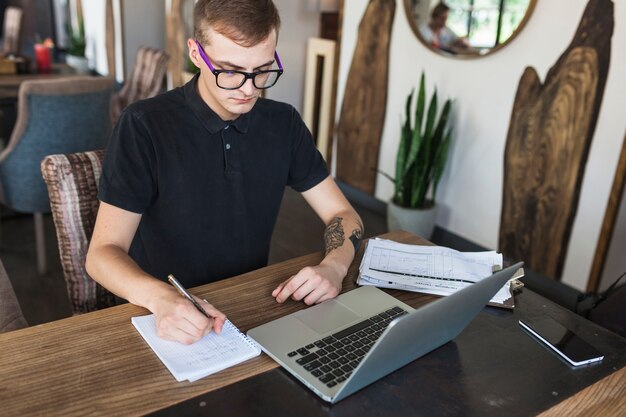 Homme assis avec bloc-notes et ordinateur portable à la table