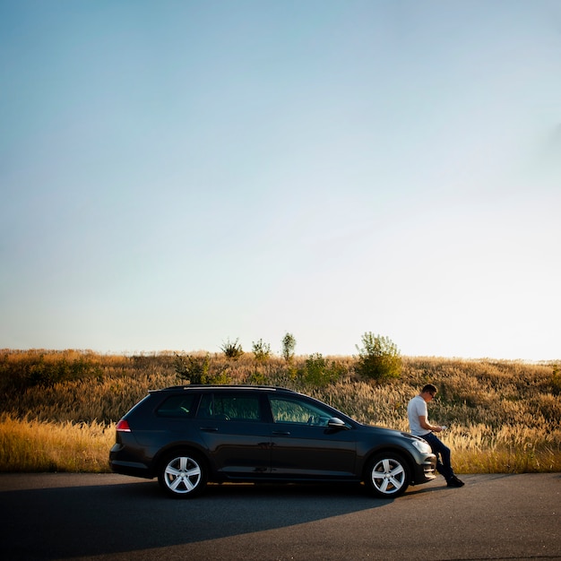 Photo gratuite homme assis sur le capot de la voiture