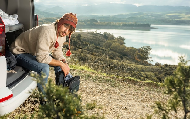 Homme assis sur le coffre de la voiture lors d'un road trip