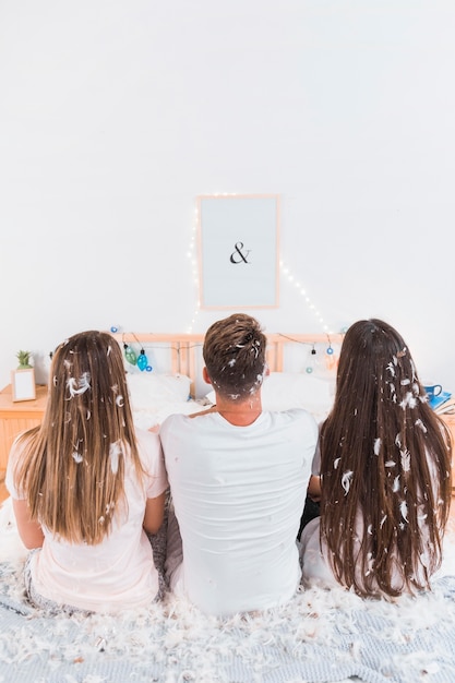 Homme assis avec deux femmes avec beaucoup de plumes sur le lit