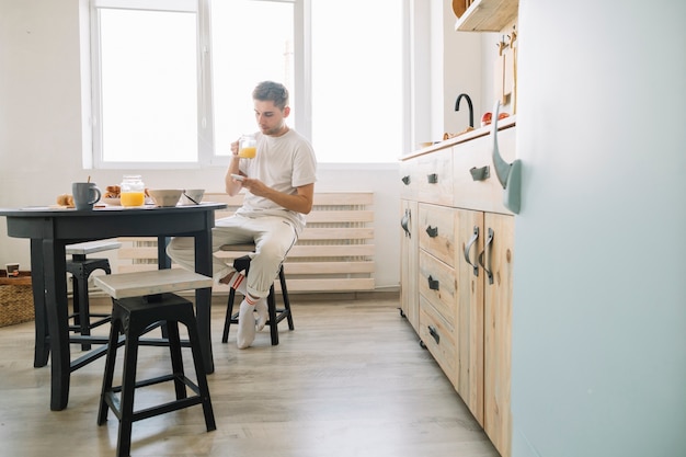 Homme assis devant une table à manger ayant du jus avec un téléphone portable