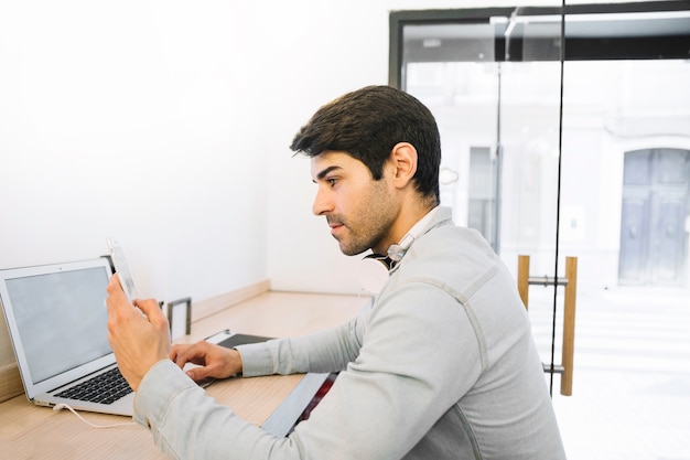 Homme assis sur un ordinateur portable en utilisant un smartphone