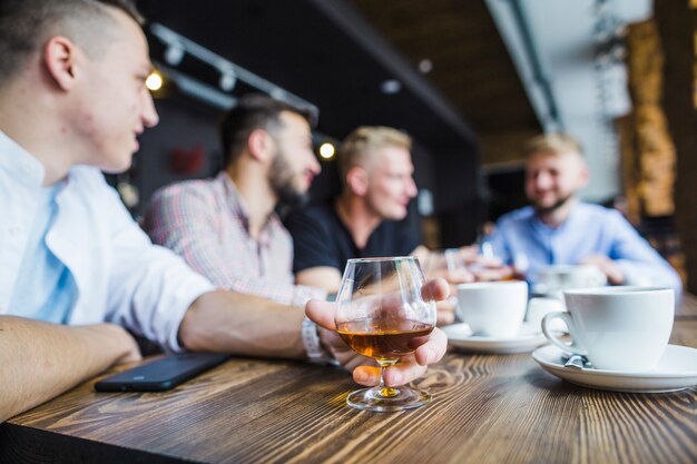 Homme assis avec ses amis dans le restaurant tenant une boisson