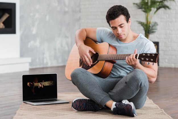 Homme assis sur le sol, apprendre à jouer de la guitare